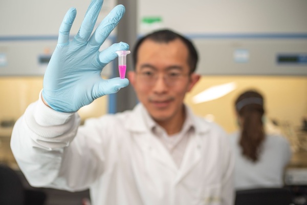 Donny Hanjaya-Putra assistant professor of aerospace and mechanical engineering holds a vial of specially engineered nanoparticle backpacks
