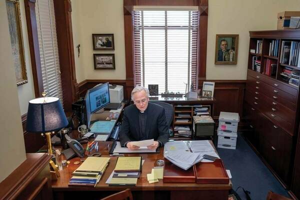 Rev. John I. Jenkins, CSC, ’76, ’78M.A., who led Notre Dame as President since 2005, prepares to step down as president on June 1. He sits at his desk sorting through papers.
