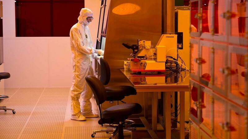 A scientist in a white suit lab suit uses tools in a Clean Room.