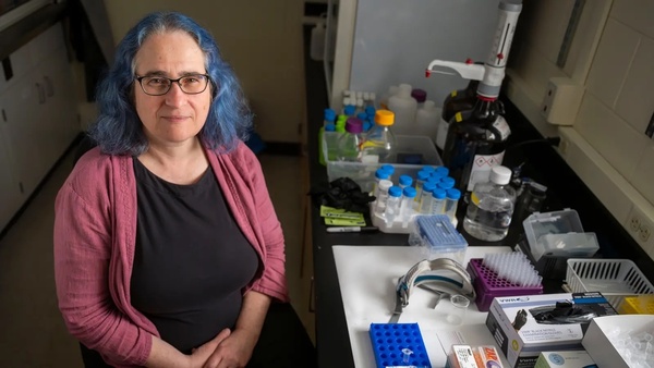 Marya Lieberman, wearing a black top with a pink sweater, smiles next to a set of samples.