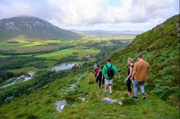 Students walking in a line down a steep green hill.