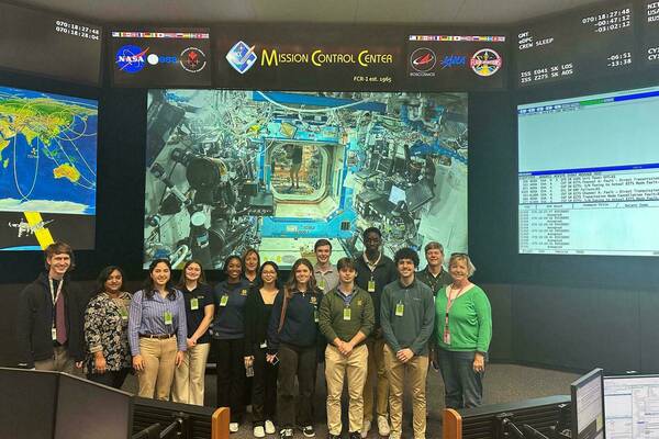 Students and hosts on the Space Trek visit NASA's Mission Control Center at Johnson Space Center with a video feed of NASA astronauts Sunita Williams and Don Pettit aboard the International Space Station in the background