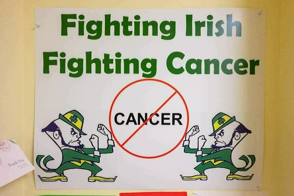 "Fighting Irish Fighting Cancer" poster. Two Notre Dame leprechaun mascots flank a red "no" symbol over the word CANCER.